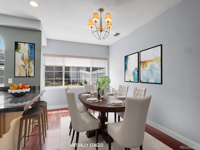 dining space featuring visible vents, a notable chandelier, baseboards, and wood finished floors