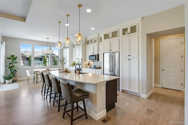 kitchen featuring baseboards, light wood finished floors, a kitchen breakfast bar, stainless steel appliances, and a kitchen island with sink