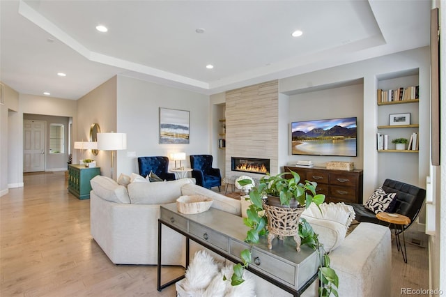 living room featuring a tray ceiling, light wood finished floors, a fireplace, and recessed lighting