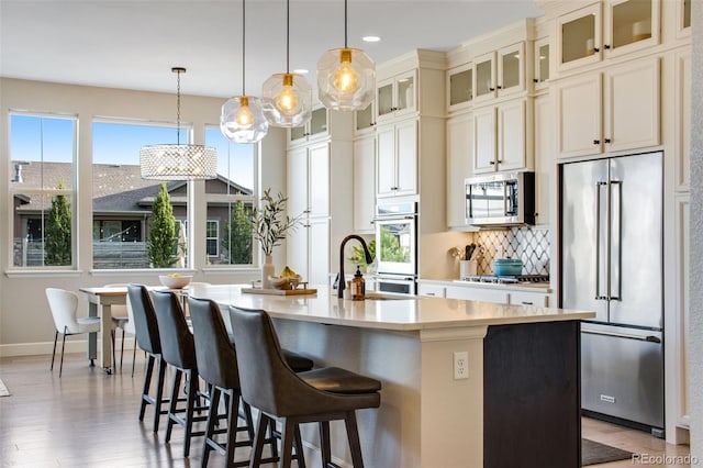 kitchen with decorative light fixtures, a breakfast bar, a center island with sink, light countertops, and appliances with stainless steel finishes
