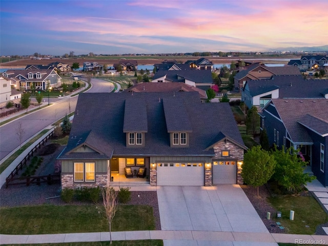 view of front of house featuring an attached garage, stone siding, a residential view, concrete driveway, and a shingled roof