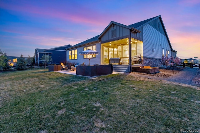 back of property at dusk with a yard, board and batten siding, an outdoor hangout area, a patio area, and stone siding
