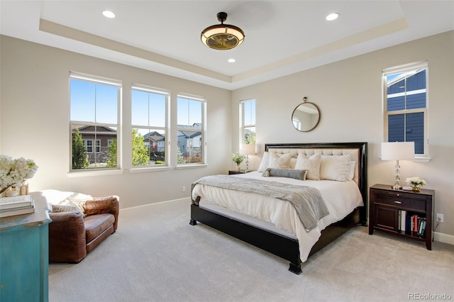 bedroom featuring light colored carpet, a raised ceiling, and baseboards