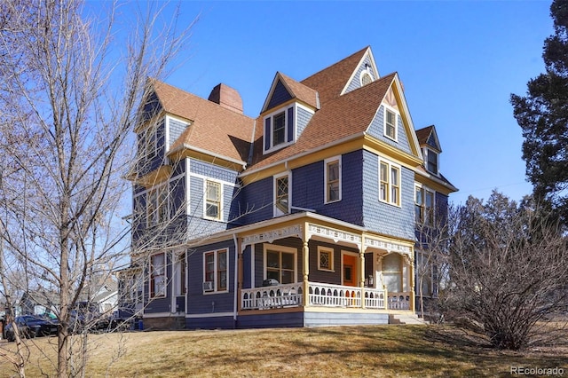 view of front of house with covered porch, a shingled roof, and a front lawn