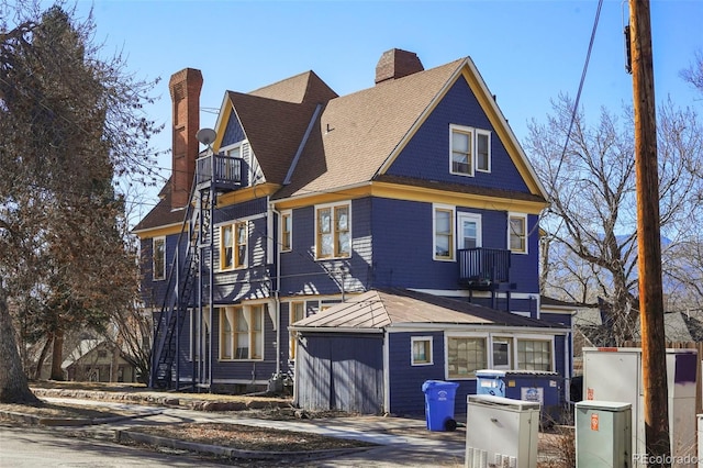 exterior space with a balcony, a chimney, and roof with shingles