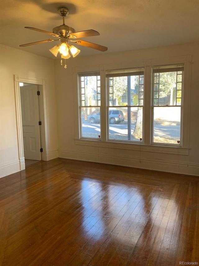 unfurnished room with dark wood-style flooring, a ceiling fan, and baseboards