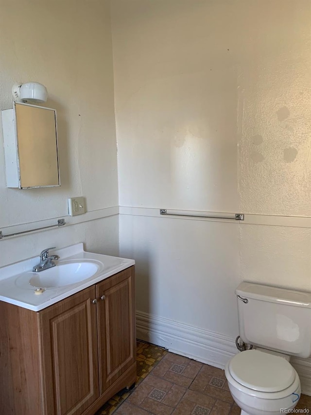 half bathroom with toilet, baseboards, and vanity