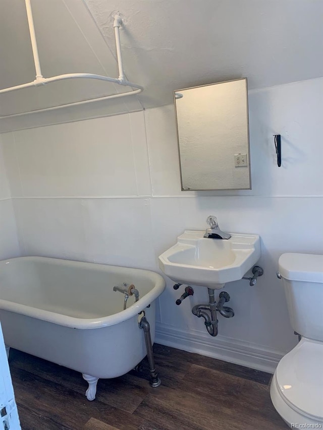 full bath featuring toilet, a freestanding bath, and wood finished floors