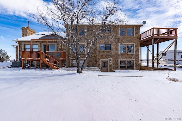 snow covered property featuring a deck, a chimney, stairs, and central air condition unit