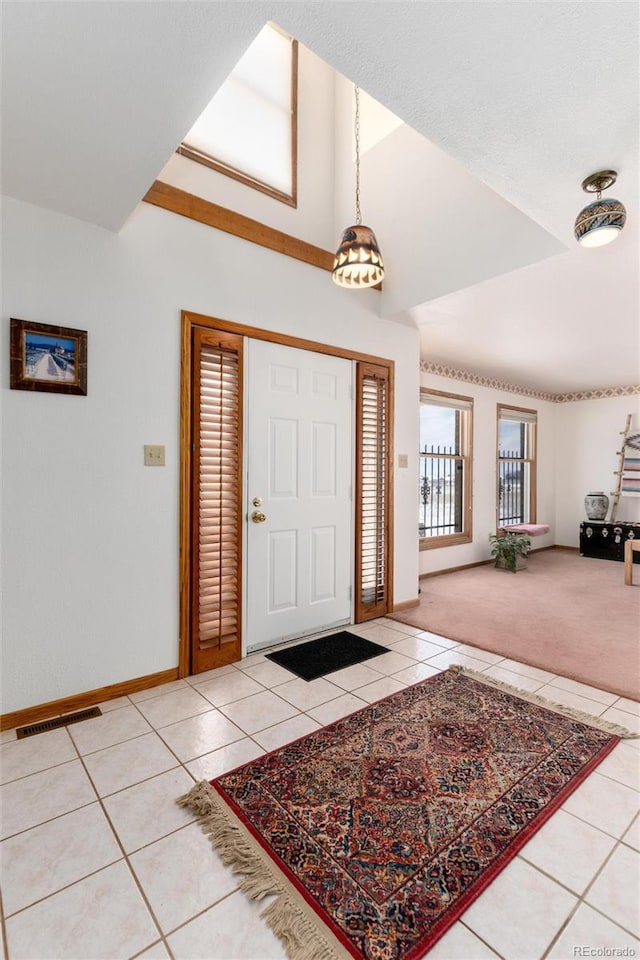 foyer entrance with light colored carpet, visible vents, baseboards, and light tile patterned floors