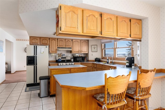 kitchen with a peninsula, wallpapered walls, white refrigerator with ice dispenser, and a sink