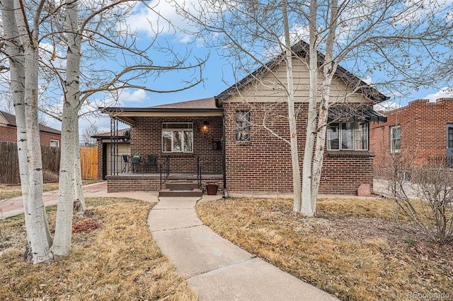 bungalow-style house with covered porch, brick siding, and fence