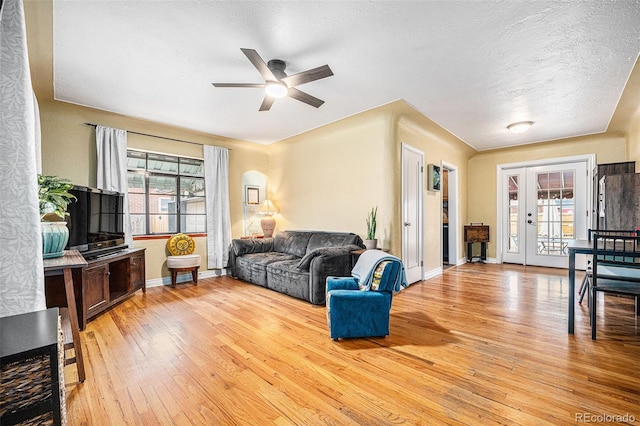 living area featuring light wood finished floors, baseboards, ceiling fan, a textured ceiling, and french doors