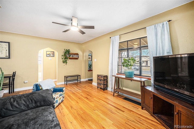 living area featuring a ceiling fan, arched walkways, baseboards, and light wood finished floors