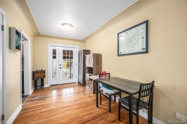 dining room with light wood-type flooring, french doors, a textured ceiling, and baseboards