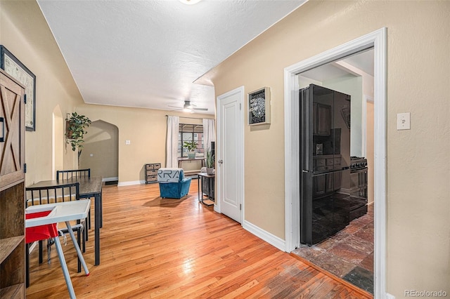 corridor with arched walkways, light wood-style flooring, and baseboards