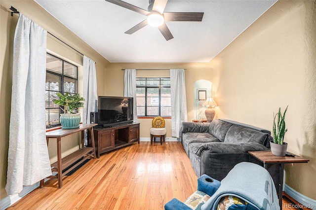 living room featuring arched walkways, ceiling fan, light wood finished floors, and baseboards