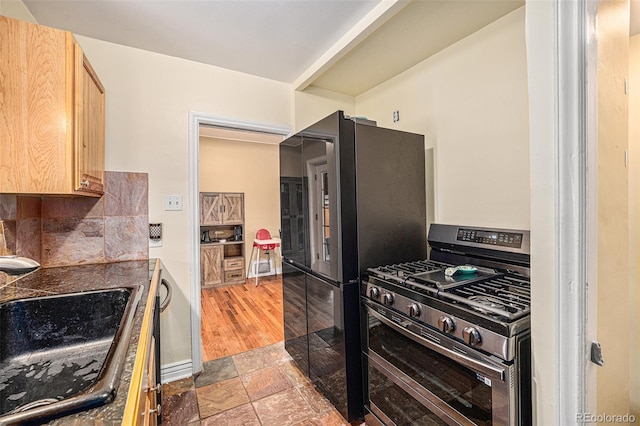 kitchen with tasteful backsplash, range with two ovens, stone tile flooring, light brown cabinetry, and a sink