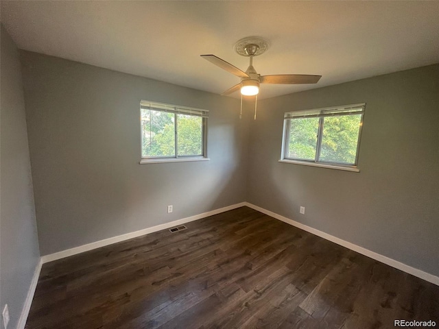 spare room featuring a healthy amount of sunlight, dark wood-style flooring, baseboards, and visible vents