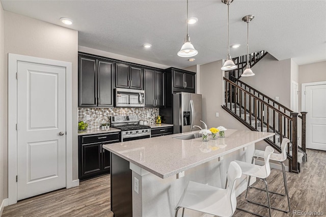 kitchen featuring stainless steel appliances, sink, a kitchen island with sink, pendant lighting, and light wood-type flooring