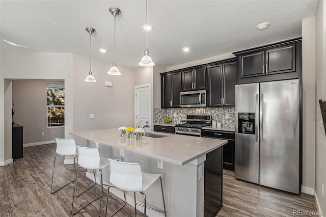 kitchen featuring wood-type flooring, appliances with stainless steel finishes, hanging light fixtures, sink, and an island with sink