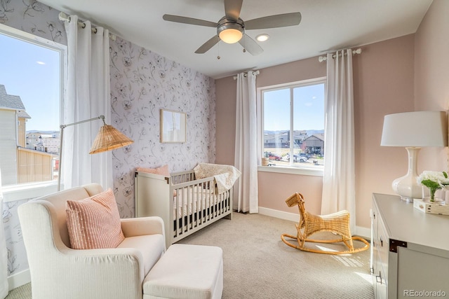bedroom with a nursery area, baseboards, light colored carpet, wallpapered walls, and a ceiling fan