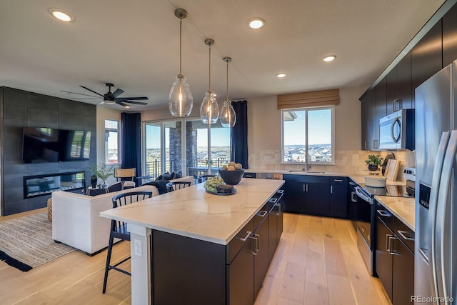 kitchen featuring appliances with stainless steel finishes, a sink, a kitchen bar, a kitchen island, and light wood-type flooring