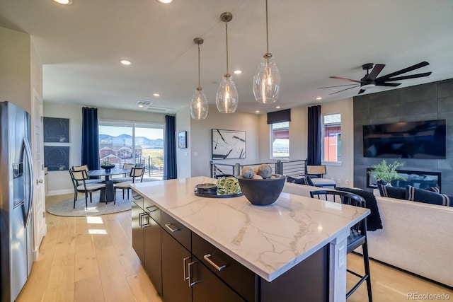 kitchen with stainless steel refrigerator with ice dispenser, open floor plan, a breakfast bar, light wood finished floors, and recessed lighting