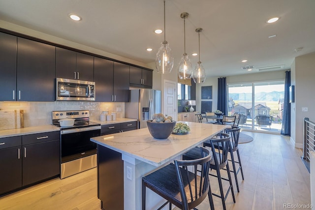 kitchen featuring stainless steel appliances, a breakfast bar, a kitchen island, recessed lighting, and light wood finished floors