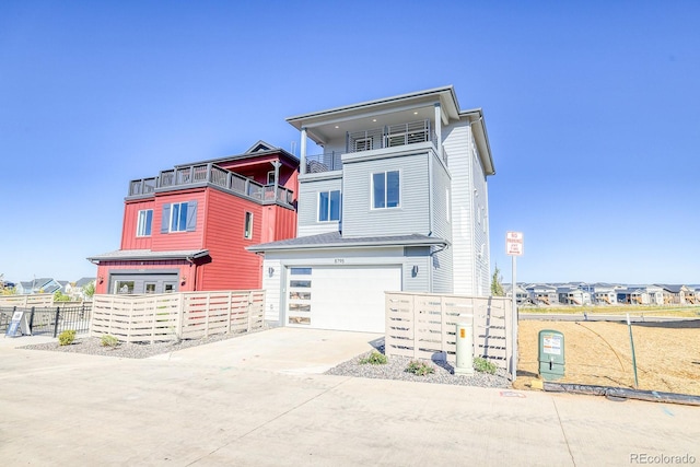 view of front of house featuring driveway, a garage, a balcony, fence, and a residential view