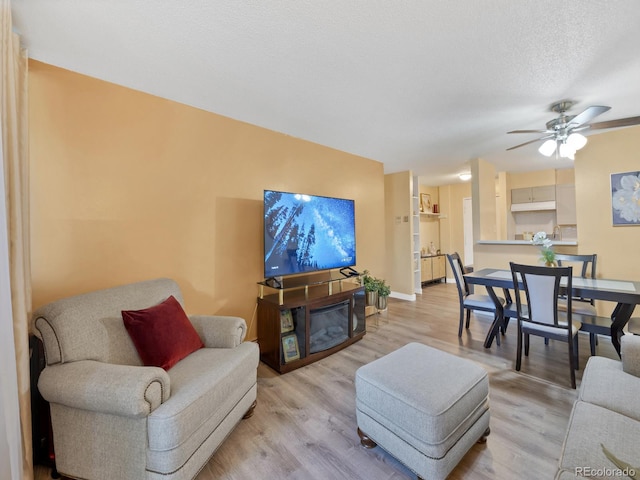 living room with ceiling fan, a textured ceiling, and light wood-type flooring