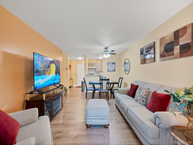 living room with light wood-type flooring, a textured ceiling, and ceiling fan