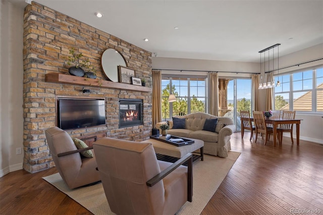 living room with baseboards, plenty of natural light, a stone fireplace, and wood finished floors