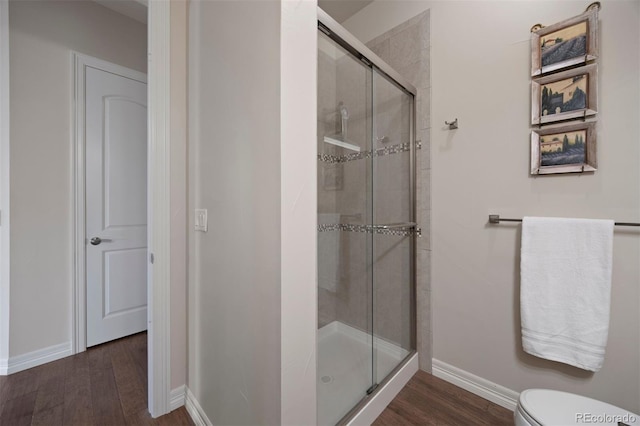 bathroom with baseboards, a stall shower, toilet, and wood finished floors
