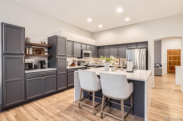 16179 W 70th Pl, Arvada, CO 80007 - kitchen with appliances with stainless steel finishes, backsplash, open shelves, an island with sink, and a breakfast bar