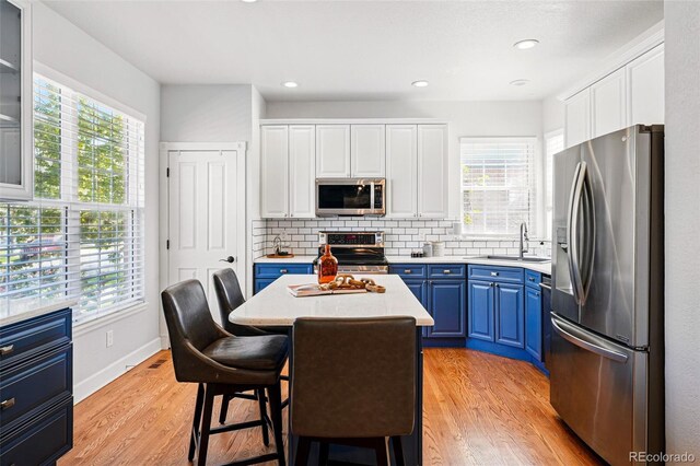 1063 Roslyn Ct, Denver, CO 80230 - kitchen featuring appliances with stainless steel finishes, blue cabinetry, a sink, a kitchen island, and light countertops