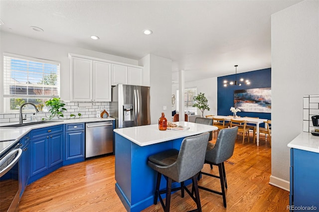 1063 Roslyn Ct, Denver, CO 80230 - kitchen with stainless steel appliances, blue cabinetry, a sink, light wood-style floors, and a kitchen breakfast bar
