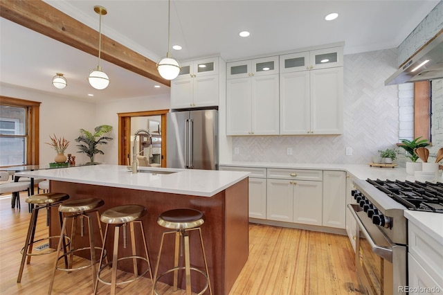 kitchen featuring premium appliances, a sink, light wood finished floors, tasteful backsplash, and recessed lighting