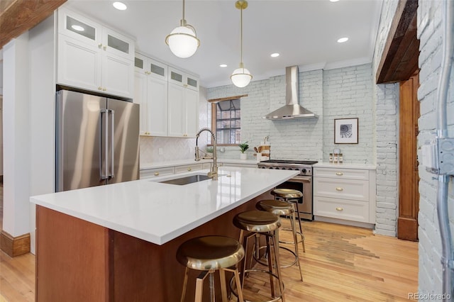 kitchen with premium appliances, wall chimney exhaust hood, light wood-style floors, a sink, and backsplash