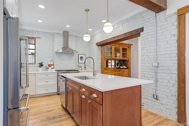 kitchen featuring wall chimney range hood, a sink, stainless steel appliances, brick wall, and light countertops
