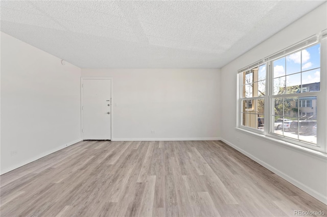unfurnished room with a textured ceiling, light wood-type flooring, and baseboards