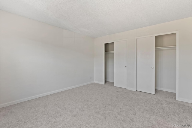 unfurnished bedroom with multiple closets, carpet flooring, a textured ceiling, and baseboards