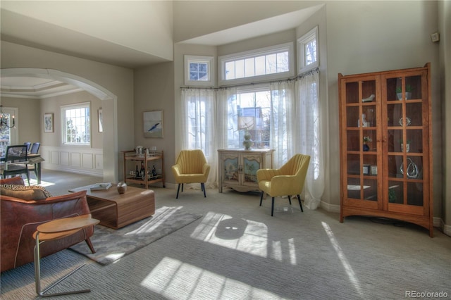 living area featuring arched walkways, a wainscoted wall, crown molding, carpet flooring, and a decorative wall