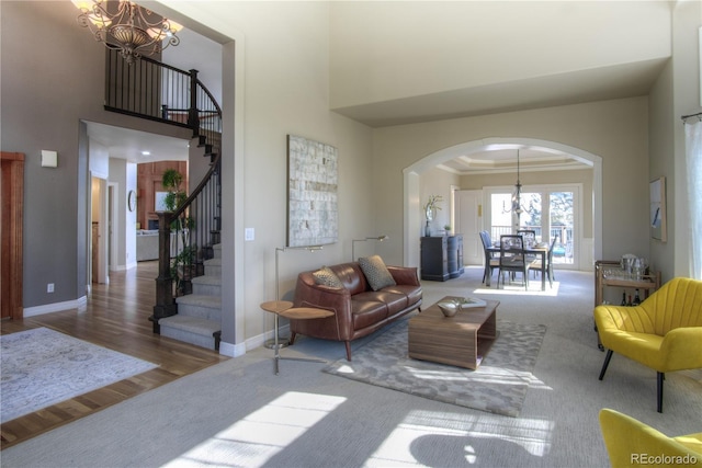 carpeted living room with arched walkways, crown molding, stairway, and an inviting chandelier