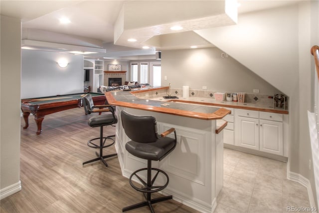 kitchen featuring a peninsula, a breakfast bar, a fireplace, white cabinets, and open floor plan