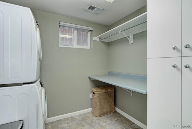 laundry room with cabinets and stacked washer and clothes dryer