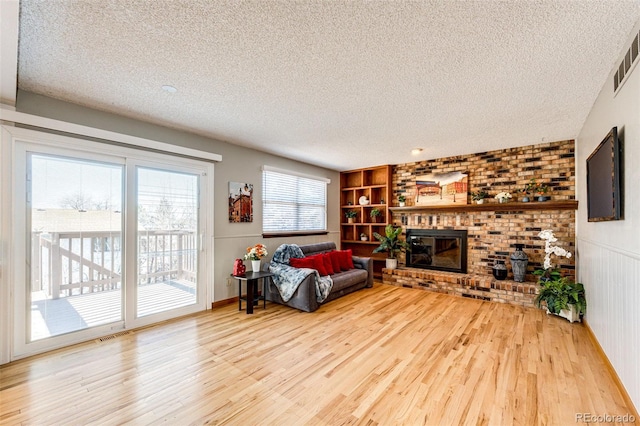 living room featuring light wood-type flooring, a textured ceiling, a brick fireplace, and built in features