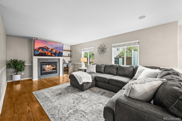 living room featuring wood finished floors, a tiled fireplace, beverage cooler, and baseboards