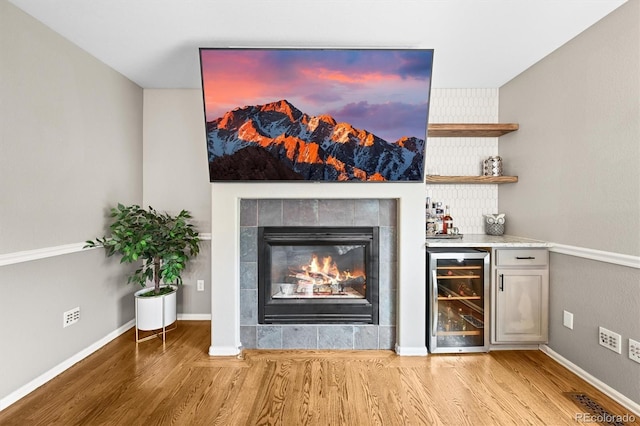 indoor dry bar with wine cooler, wood finished floors, a tile fireplace, and baseboards