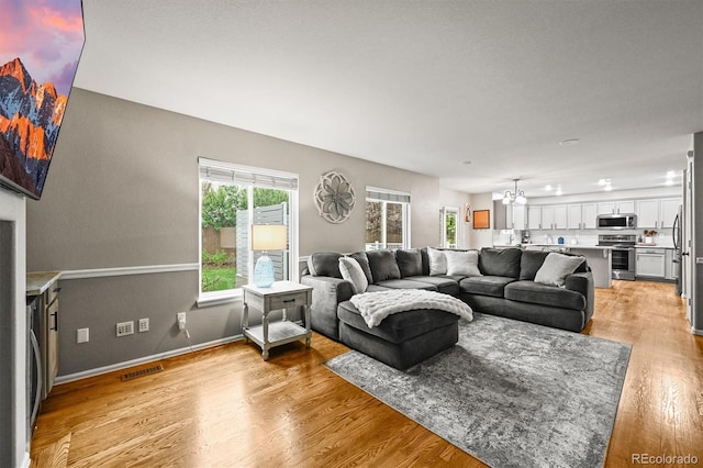 living area featuring a chandelier, light wood-style floors, and baseboards